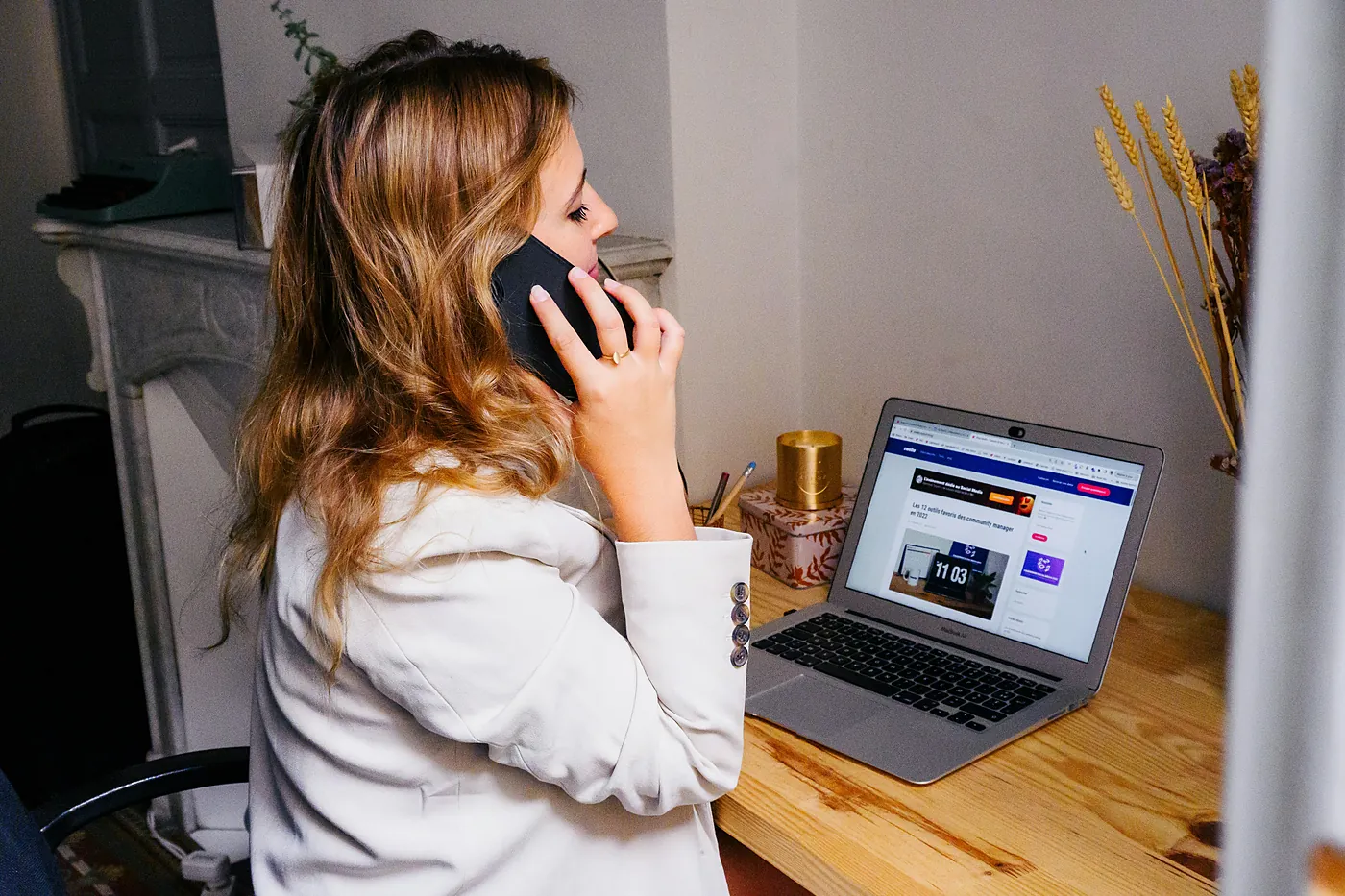 A woman on her phone at a desk with a laptop