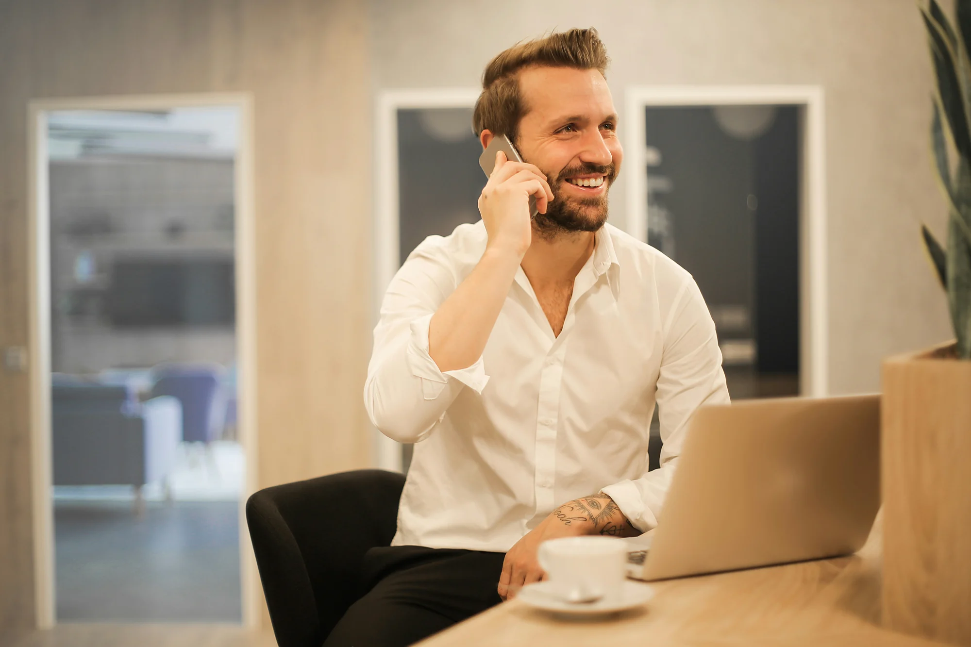 A smiling man in a white shirt on a phone call at his laptop